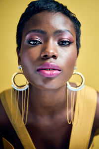 Close-up portrait of young woman with big earrings and yellow background 
