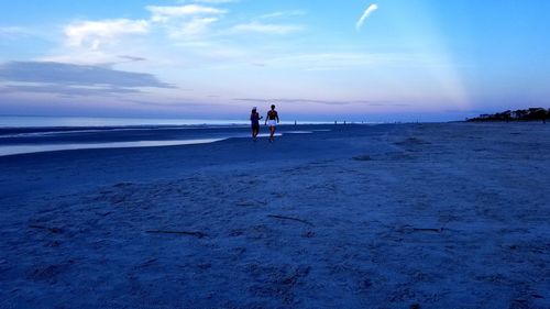 Rear view of people walking at beach against sky during sunset