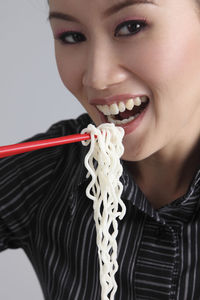 Portrait of woman eating noodles with chopsticks against white background