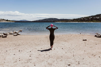 Rear view of woman standing at beach against sky