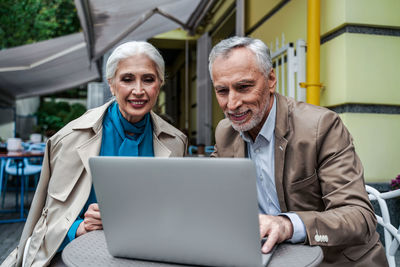 Smiling senior couple video calling while sitting at cafe