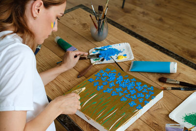 Woman artist painting picture at home with acrylic paints and spatula. adult hobby
