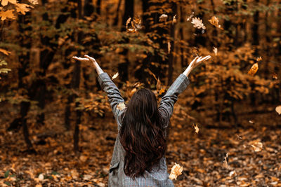 Back view of brunette woman with fall yellow leaves in long hair on autumn nature background