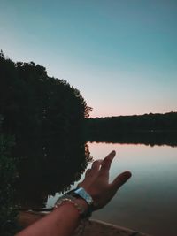 Midsection of person by lake against sky during sunset