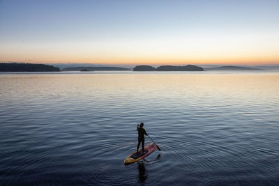 Person in sea against sky during sunset