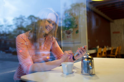 Smiling woman using mobile phone while sitting at cafe