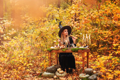 Young woman sitting by plants in autumn