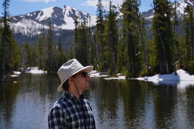 Side view of man standing by lake against mountains during winter