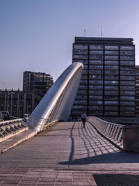 Rear view of man walking on bridge against buildings in city