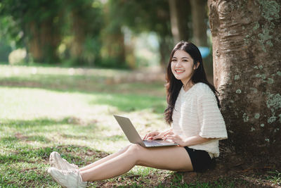 Young woman using laptop while sitting on field