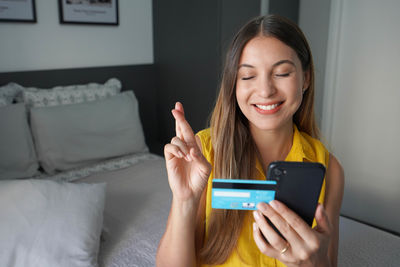 Woman keeps fingers crossed expresses a wish holds phone and credit card waits for dreams come true