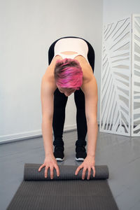 A young woman with pink hair lays out a yoga mat or pilates mat.