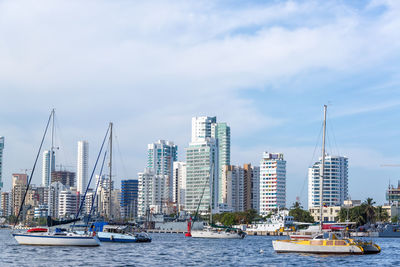 Sailboats sailing in sea against buildings in city