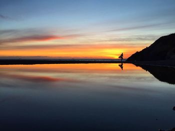 Silhouette man carrying surfboard while walking on beach during sunset