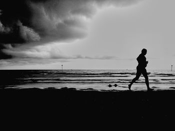 Silhouette man walking on beach against sky