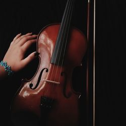 Cropped hand of woman touching violin in darkroom