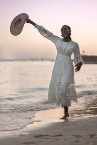 Beautiful african woman in sun hat walks on beach at sunset. 