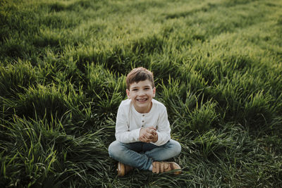 Cheerful boy with hands clasped sitting at grassy field