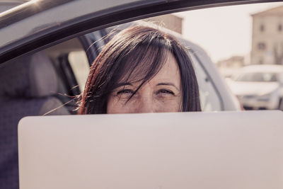 Portrait of woman using laptop sitting by car door