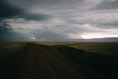 Tire tracks on agricultural field against storm clouds