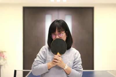 Portrait of young woman holding table tennis racket at home