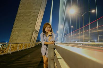 Smiling woman standing on illuminated bridge at night