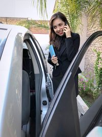 Woman using mobile phone while standing by car