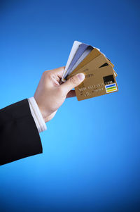 Cropped hand holding credit cards against blue background