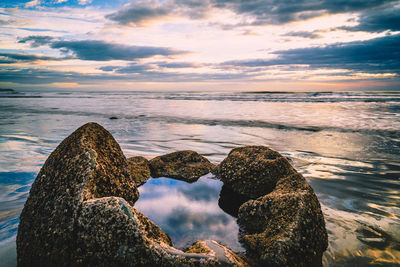 Rocks on beach against sky during sunset