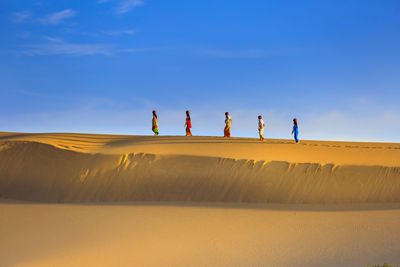 People on sand dune in desert against sky