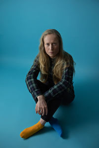 Portrait of young woman sitting against blue background