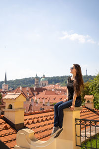 Full length of woman sitting on wall against townscape