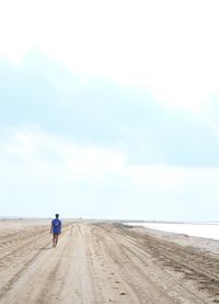 Rear view of man walking at beach against sky