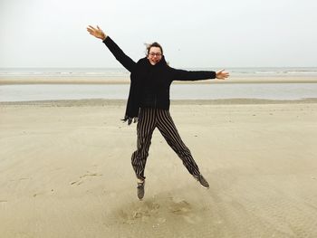 Full length of woman with arms raised on beach against sky