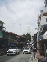 Cars on city street by buildings against sky