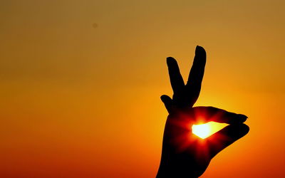 Cropped image of silhouette hand doing gyan mudra against sky during sunset