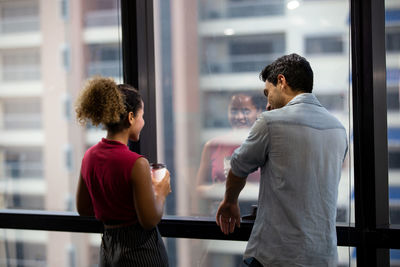 Rear view of business colleagues talking while standing against window at office