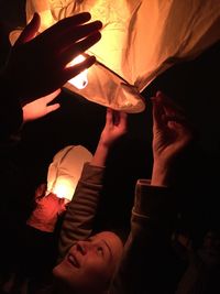 People with arms raised amidst burning paper lantern at night