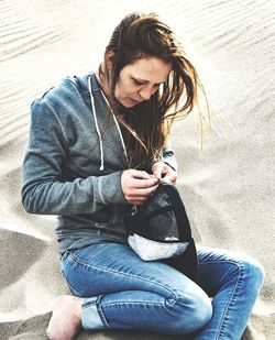  mid adult woman holding cap while sitting on sand at beach