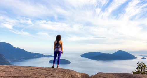 Rear view of woman standing on rock against sky