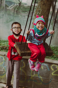 Full length of boy swinging his little sister sitting on swing at playground