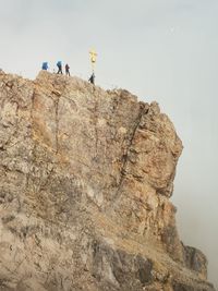 Low angle view of people by cross on rocky mountains against sky