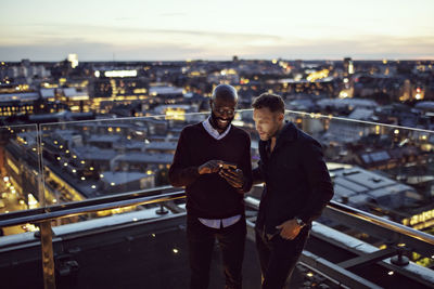 Smiling businessman showing smart phone to coworker on terrace after office work in city