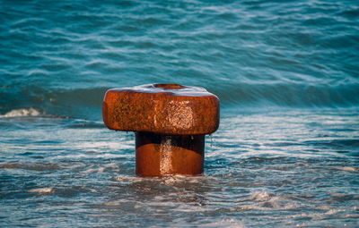 Close-up of rusty metal on wooden post in sea