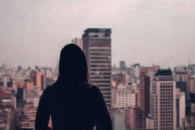 Rear view of man looking at city buildings against sky