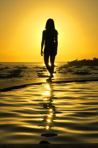 Silhouette woman standing at beach against sky during sunset