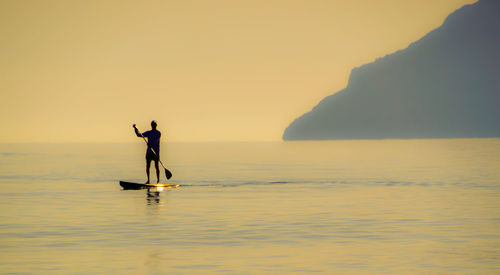 Silhouette man standing in sea against sky during sunset