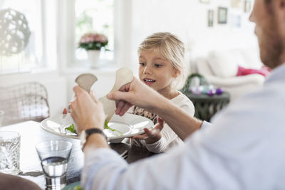 Father serving salad to daughter at dining table