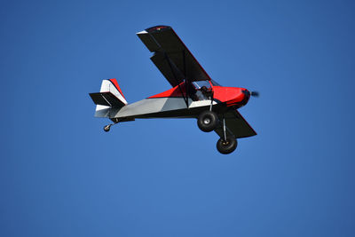 Low angle view of propeller airplane flying against clear blue sky