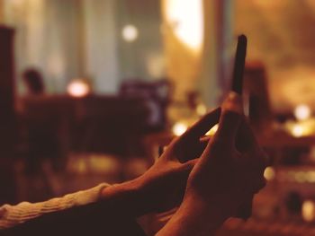 Cropped hands of woman holding smart phone in illuminated room